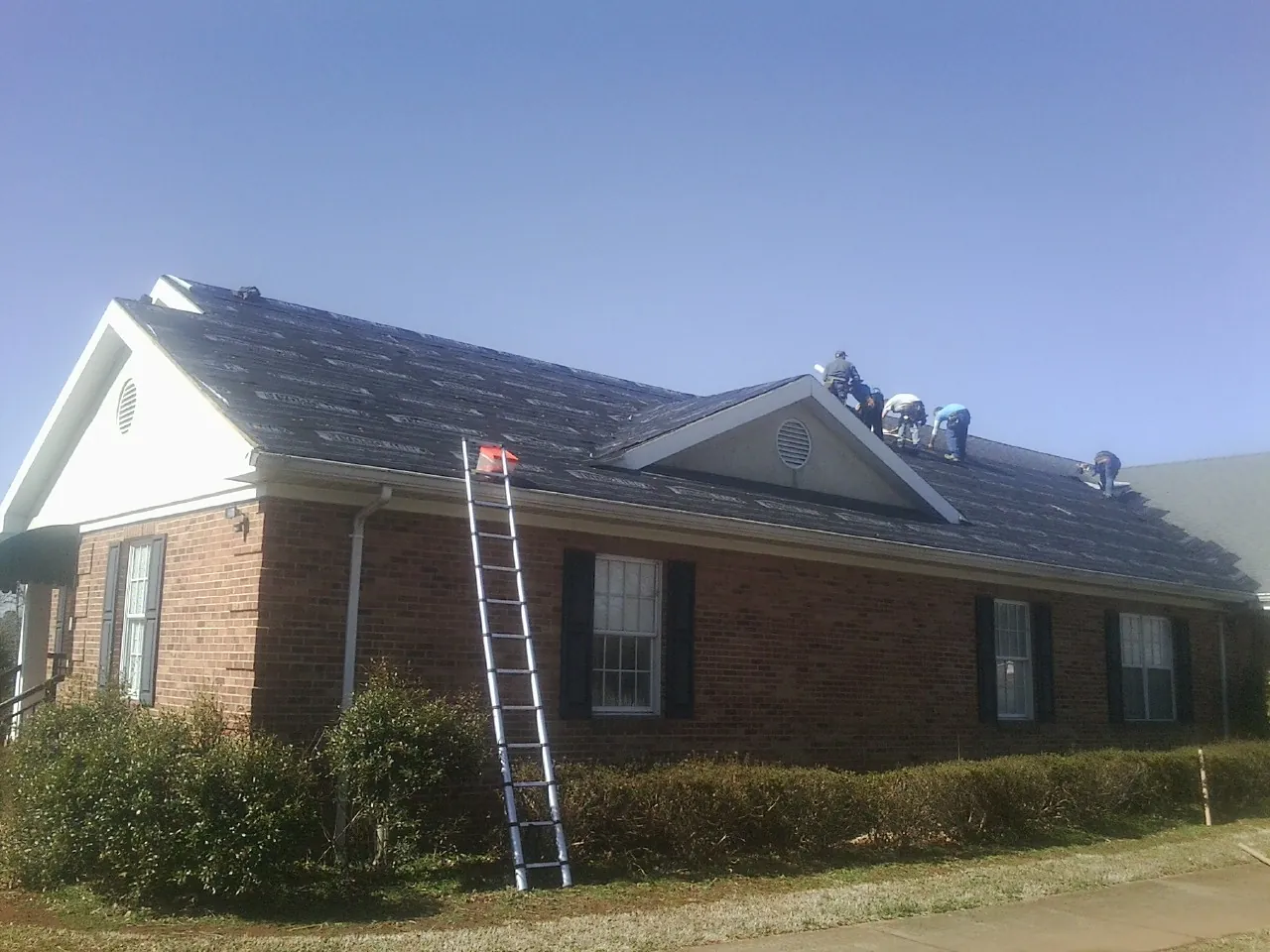 Crew tearing shingles off a brick ranch roof with a ladder set — Emergency Roof Repair work by our crew in Henrico