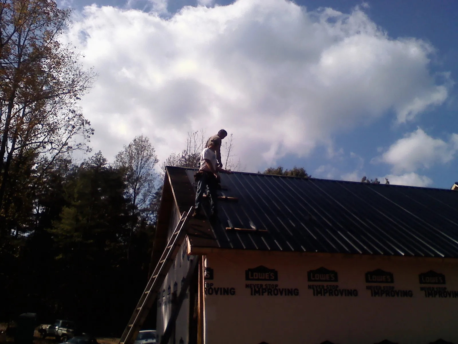 Roofer fastening dark metal panels high against a cloudy sky, from a Roof Inspection job in Henrico